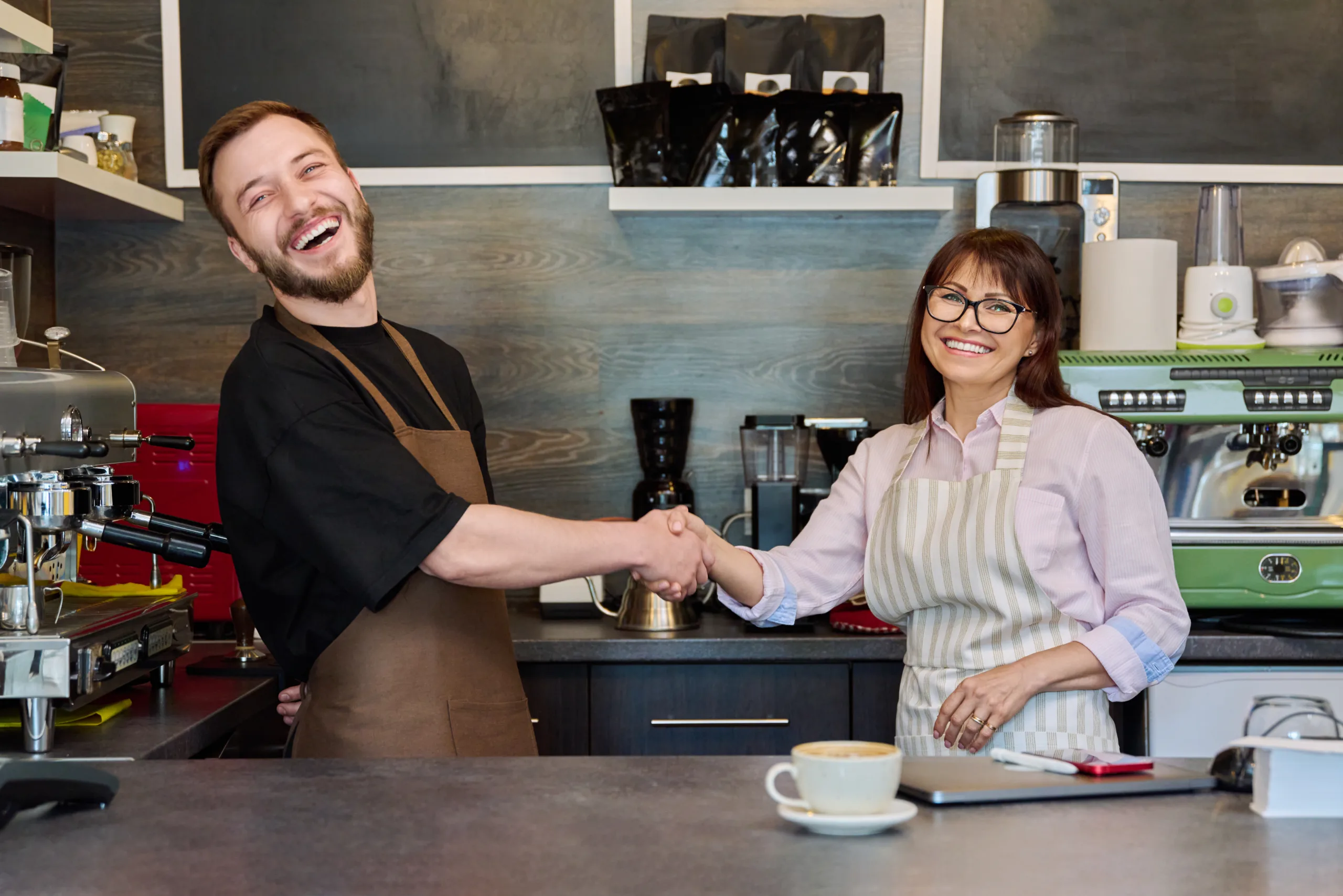 Colleagues, partners, man and woman shake hands, in coffee shop near counter. Team, small business, work, staff, teamwork, entrepreneurship, partnership concept
