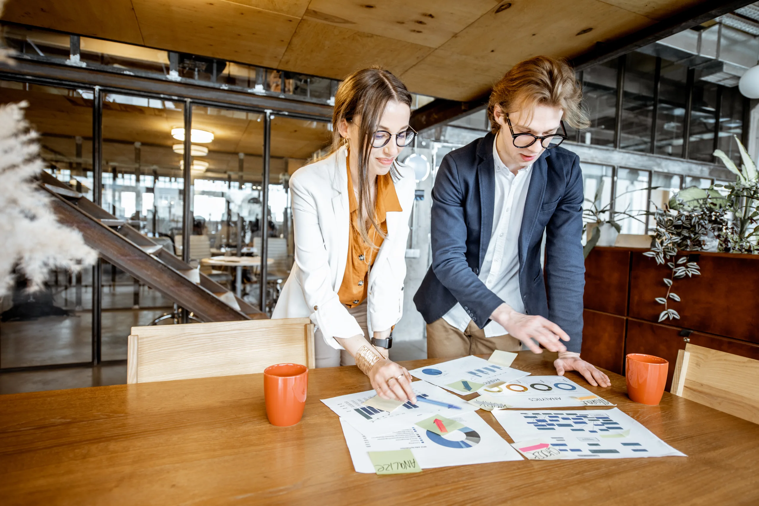 Young business man and woman working on documents at the wooden table in the office or coworking space